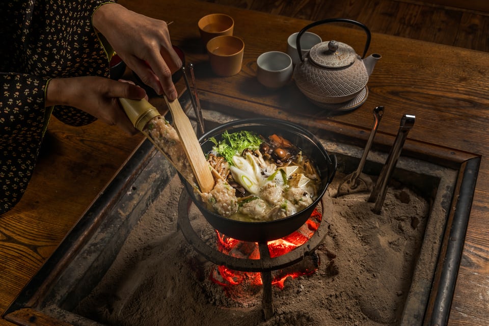 趣ある囲炉裏で郷土料理の鍋料理をしている女性